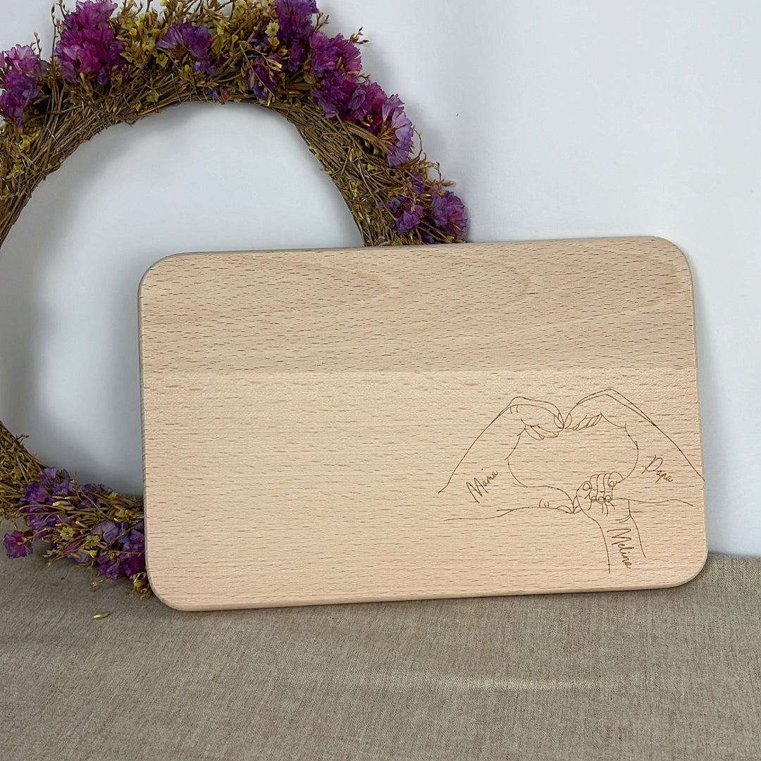 Personalisiertes Schneidebrett aus Holz mit graviertem Herzmotiv aus Händen und individuellen Namen – ideales Geschenk für Familien oder Freund:innen
