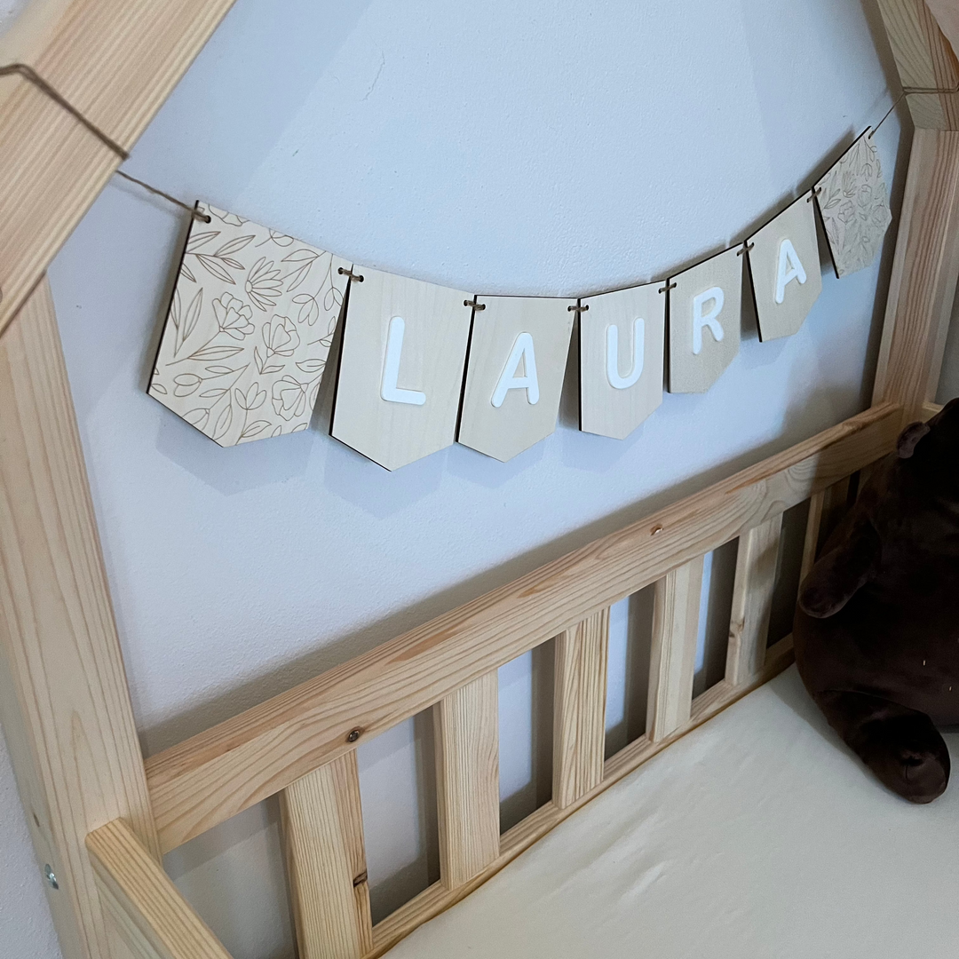 Personalisierte Wimpelkette aus Holz mit dem Namen „Laura“, aufgehängt über einem Kinderbett – perfekt als Kinderzimmer-Deko